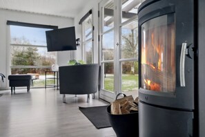 Ein modernes Interieur mit Kaminofen, großen Fenstern, einem Flachbildfernseher und einem schwarzen Sessel.