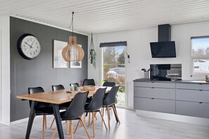 Eine moderne Küche mit Essbereich, ausgestattet mit einem Holztisch, schwarzen Stühlen, einer Uhr, Pendelleuchten und einem großen Fenster.
