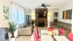 A living room with a stone fireplace, a ceiling fan, a dining table with red chairs, and a sofa. - Spacious Retreat in Prime Location — Comfort, Style & Convenience” (Owings Mills)