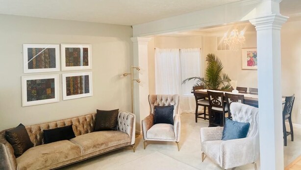 A spacious living room with a beige sofa, a tufted armchair, and a white armchair. There is a dining area with a table and chairs in the background. - Spacious Retreat in Prime Location — Comfort, Style & Convenience” (Owings Mills)