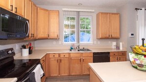 A kitchen with wooden cabinets, a black microwave, a sink, and a window with a view of trees. - Spacious Retreat in Prime Location — Comfort, Style & Convenience” (Owings Mills)