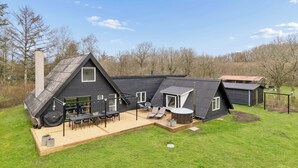 A modern house with a large deck, a chimney, and a small attached building. - Holiday home with spa, sauna and hot tub (Farsø)