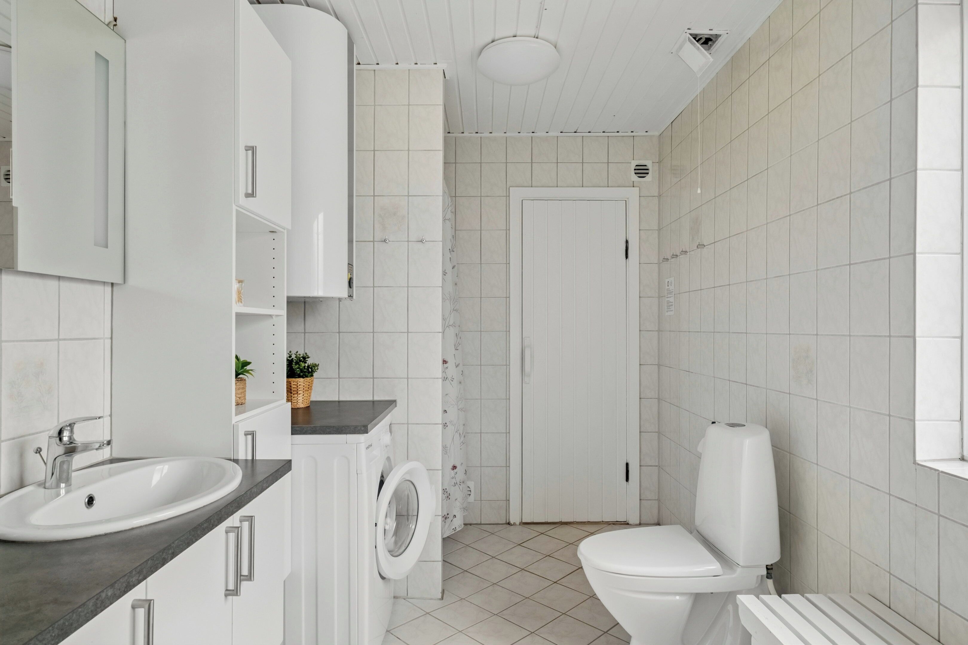 Un baño con lavamanos, lavadora, inodoro y cortina de ducha.