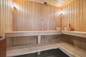 Een sauna met houten wanden en banken, een bank met een emmer, en een stenen wasbak.