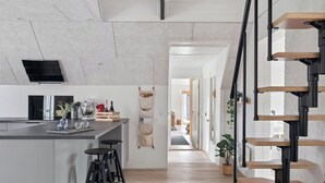 A modern kitchen with a central island, bar stools, a hanging apron, and a staircase with wooden steps. - Holiday home with spa, sauna and hot tub (Farsø)