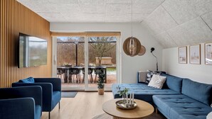 A modern living room with a blue sofa, a wooden coffee table, and a TV mounted on the wall. - Holiday home with spa, sauna and hot tub (Farsø)