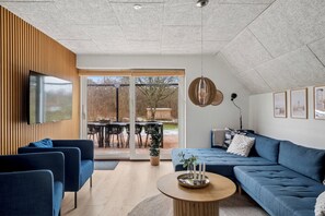 A modern living room with a blue sofa, a wooden coffee table, and a TV mounted on the wall. - Holiday home with spa sauna and hot tub (Farsø)