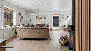 A cozy living room with a sofa, a fireplace, and a dining area with a table and chairs. - Holiday home with spa, sauna and hot tub (Farsø)