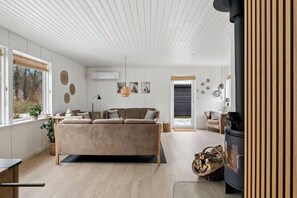 A cozy living room with a sofa, a fireplace, and a dining area with a table and chairs. - Holiday home with spa sauna and hot tub (Farsø)