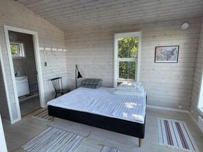 Ein Schlafzimmer mit Bett, Stuhl, Schreibtisch, Fenster und einem Bild an der Wand.