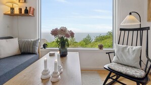 A room with a view of the sea, a wooden table with candles, a black rocking chair, and a sofa. - Holiday home with stunning Baltic Sea view (Hasle)