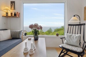Ein Zimmer mit Meerblick, ein Holztisch mit Kerzen, ein schwarzer Schaukelstuhl und eine Couch.