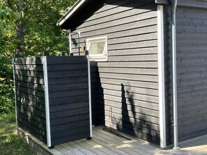 A wooden building with a dark exterior, a small window, and a metal door. - Holiday home with stunning Baltic Sea view (Hasle)