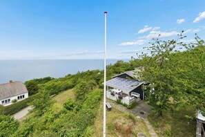 Ein Küstenhaus mit Solardach, einer Fahnenstange und Blick auf das Meer.