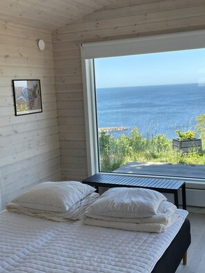 Une chambre avec un lit, une fenêtre donnant sur la mer et un mur en bois.