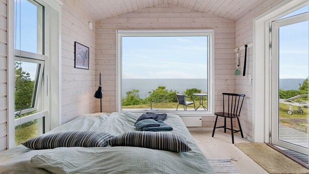 A bedroom with a large window, a bed with pillows, a chair, and a small table. - Holiday home with stunning Baltic Sea view (Hasle)