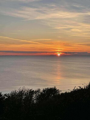 A sunset over a calm sea with a distant landmass. - Holiday home with stunning Baltic Sea view (Hasle)