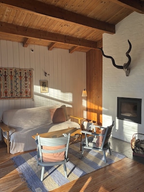 A cozy room with a bed, a wooden table, two chairs, a fireplace, and a wall-mounted TV. - Idyllic wooden cabin with fireplace near Tisvilde (Frederiksværk)