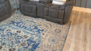 Ein Wohnzimmer mit zwei braunen Ledersesseln, einem blauen Teppich mit Muster und einem kleinen Beistelltisch.