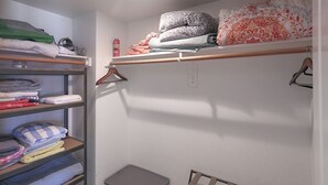 Ein Schrank mit Regalen und Kleiderstange, gefüllt mit gefalteter Kleidung und Decken.