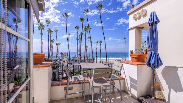 Ein Balkon mit Blick auf das Meer, Palmen und einen blauen Sonnenschirm.
