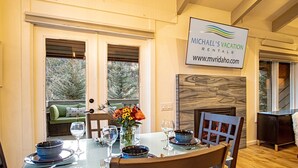 A dining area with a table set for four, a fireplace, and a sign for Michael's Vacation Rentals. - Sv124- Walk to Lifts and Town-hot tub & Pool (Ketchum)