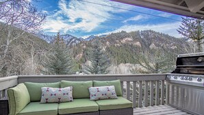 A balcony with a green cushioned sofa, a grill, and a view of a mountainous landscape. - Sv124- Walk to Lifts and Town-hot tub & Pool (Ketchum)
