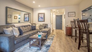 A living room with a gray sofa, a coffee table, and a wooden dining table with chairs. There is a mirror on the wall, a rug on the floor, and a door leading to another room. - Sv124- Walk to Lifts and Town-hot tub & Pool (Ketchum)
