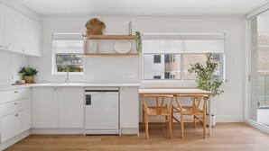 Una cocina moderna con muebles blancos, una mesa de comedor de madera y vistas de la ciudad a través de grandes ventanales.