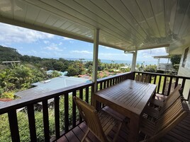 A wooden deck with a table and chairs, overlooking a coastal area with houses and greenery.