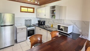 A kitchen with wooden ceiling, white cabinets, a stainless steel refrigerator, a stove, a microwave, and a dining table with chairs. - Luna's Home Raiatea (Tumaraa)