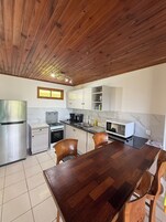 Una cocina con techo de madera, armarios blancos, un refrigerador de acero inoxidable, estufa, microondas y una mesa de comedor con sillas.