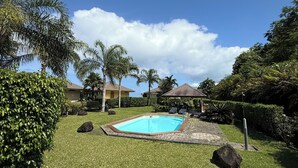A swimming pool surrounded by well-maintained grass and palm trees, with a clear blue sky above. - Luna's Home Raiatea (Tumaraa)