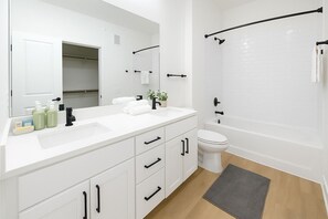 Ein modernes Badezimmer mit einem weißen Waschbecken, einem schwarzen Wasserhahn und einer Badewanne mit einem schwarzen Handtuchhalter.