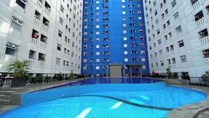 Une piscine dont le sol et les murs sont recouverts de carreaux, entourée d’un immeuble résidentiel à plusieurs étages doté de balcons et de fenêtres.