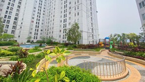A residential area with high-rise apartment buildings, a landscaped garden with a circular pathway, and playground equipment. - White Style 2Br At Bassura City Apartment (Jakarta)