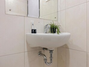 Ein Waschbecken mit Spiegel darüber, einem Wasserhahn und einem Blumentopf.