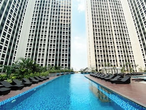 A swimming pool with lounge chairs and tall buildings in the background. - Enjoy Living Studio At Apartment Pollux Chadstone (Cikarang)