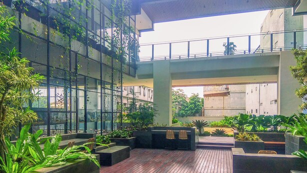 An indoor atrium with a wooden floor, planters with greenery, and a seating area with chairs. - Cozy 1Br Apartment Evenciio Margonda (Depok)
