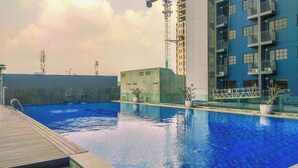 A swimming pool with a wooden deck and potted plants, surrounded by modern buildings and construction cranes. - Cozy 1Br Apartment Evenciio Margonda (Depok)
