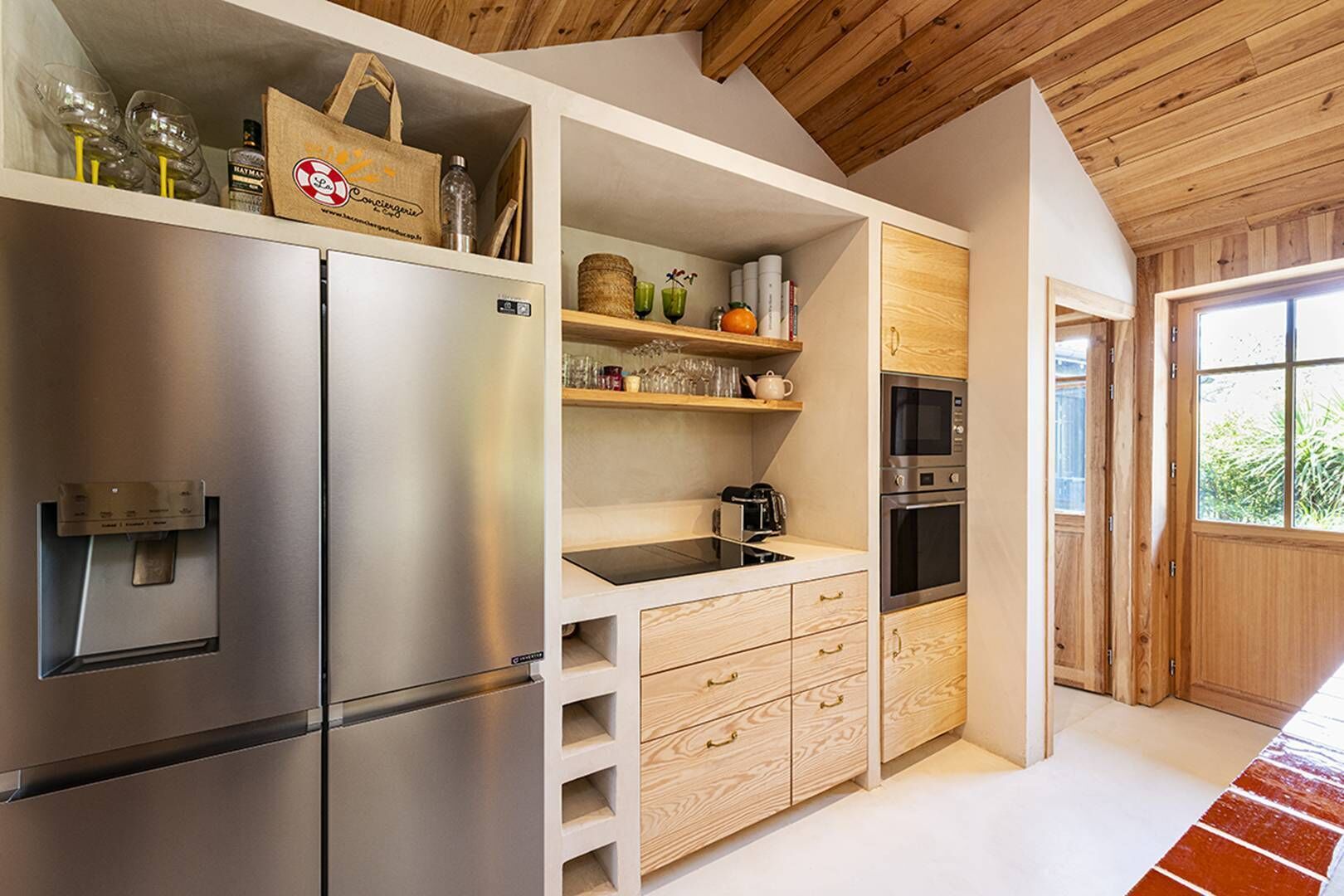 Eine moderne Küche mit einem Edelstahlkühlschrank, Holzschränken, einem Einbauofen und einem Fenster.
