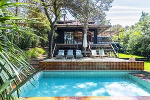 Ein Schwimmbecken mit Liegestühlen, einer Holzterrasse und einem Gebäude mit einem Ziegeldach.