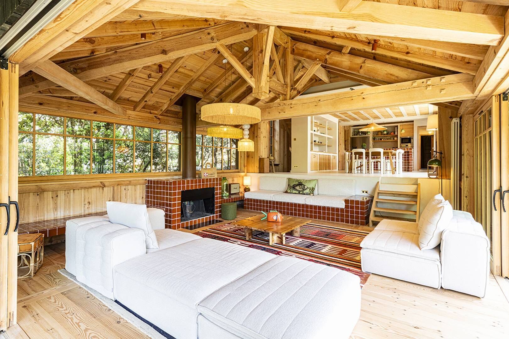A log cabin interior with a fireplace, two sofas, a dining area, and a kitchen.