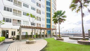 A multi-story hotel with a covered outdoor seating area, palm trees, and a view of the ocean. - Enjoy Living Studio At Apartment Sentraland Medan (Medan)