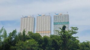 Three high-rise buildings with a dense grid of windows, surrounded by lush green trees. - Relax Studio Room Apartment At B Residence (Pagedangan)