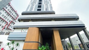 A modern high-rise building with a prominent entrance featuring a wooden column and a covered walkway. - Cozy Warm Tone Studio At Monroe Tower Apartment (Cikarang)