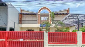 A two-story building with a red gate, a balcony, and a covered area with a glass roof. - Cozy Living Studio (No Kitchen) At Celebrity Mansion (Bekasi)