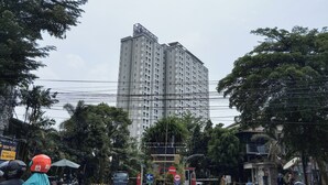A tall residential building with multiple floors and balconies, surrounded by trees and power lines. - Best View Studio At Apartment Skyland City Jatinangor (Hegarmanah)