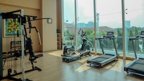 A gym with cardio equipment, weight machines, and large windows offering a city view. - Simple Designed And Homey Studio At Apartment Capitol Suites (Jakarta)