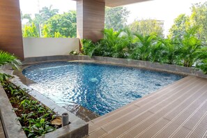 A swimming pool with a wooden deck and surrounding greenery. - Scenic And Modern Studio At Apartment Capitol Suites (Jakarta)